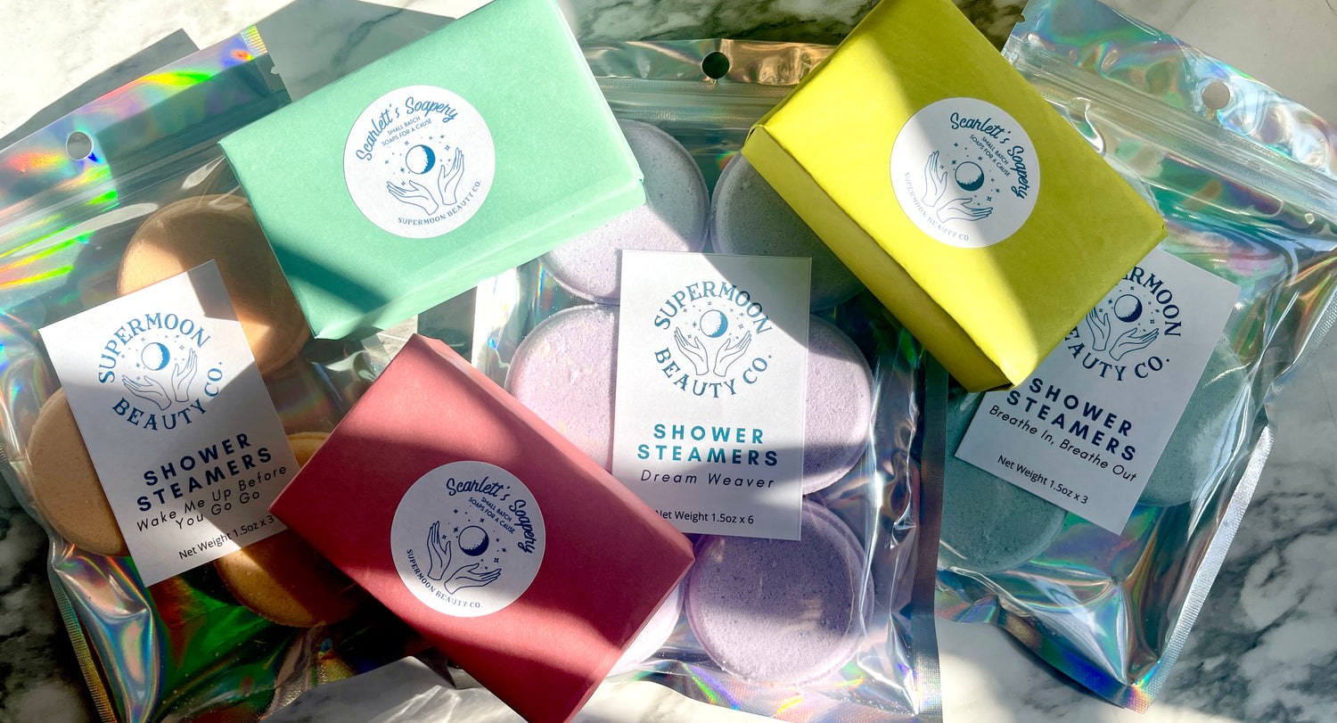 Colorful Supermoon Beauty Co. products. Soaps wrapped in paper, shower steamers in holographic packaging.